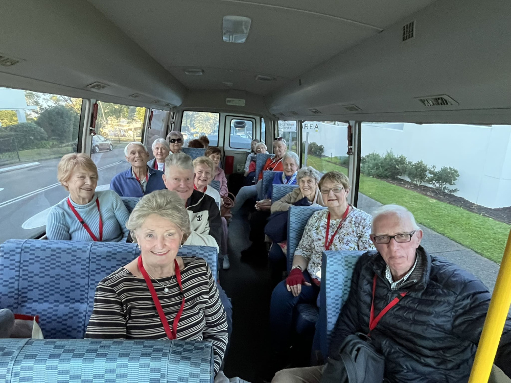Group of St George Community clients smiling together while travelling on a community bus
